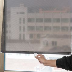 a person holding a remote control in front of a window with a mesh curtain over it