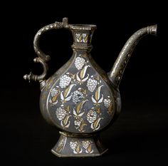 an ornately decorated silver teapot on a black background with white flowers and leaves