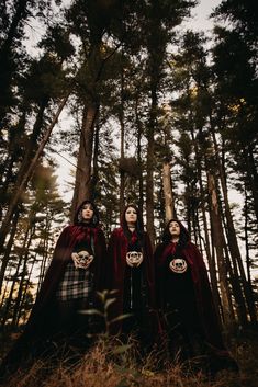 three women dressed in red cloaks standing next to each other with skulls on their faces