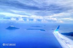 an airplane wing flying over the ocean with clouds and islands in the distance on a cloudy day