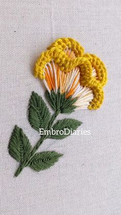 a crocheted flower with leaves is shown on a white surface, next to a green leaf