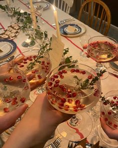 people holding wine glasses filled with food and garnished with greenery on the table