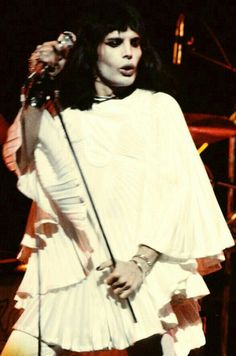 a woman with black hair and makeup holding a microphone in her right hand while standing on stage