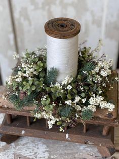 a spool of white thread sitting on top of a wooden box filled with greenery