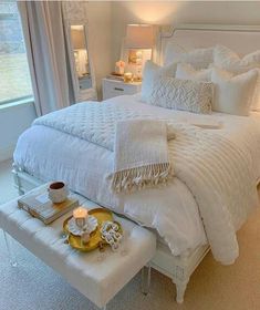 a white bed sitting in a bedroom next to a window with lots of pillows on it