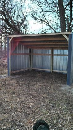 an open metal shed in the middle of a field with trees and grass around it