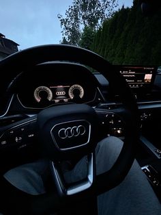 the interior of an audi car with dashboard lights and steering wheel controls, trees in the background