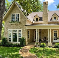 a brick house with white trim on the front and side windows, surrounded by green grass