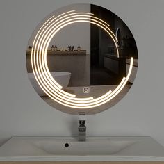 a bathroom mirror with a circular light in the middle on top of a counter next to a sink