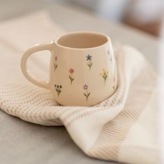 a white coffee cup sitting on top of a table next to a cloth covered napkin