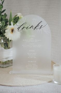 a table setting with flowers and drinks on the place card holder, along with a candle