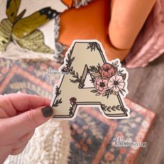 a person holding up a sticker with the letter a in floral designs on it