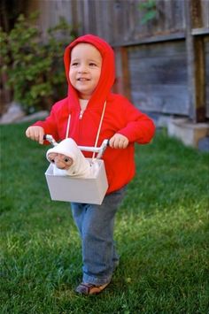 a little boy in a red hoodie is riding a bike with a bag on the handlebars