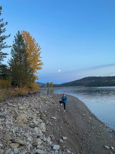 a person running along the shore of a body of water at dusk with trees in the background