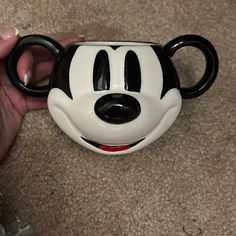 a person holding a mickey mouse coffee mug in their hand on the carpeted floor