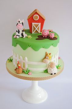 a green cake with farm animals on it and a red barn in the back ground