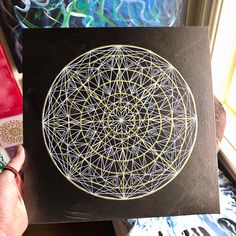 a person holding up a piece of art that looks like a flower of life on black paper