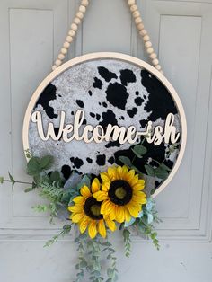 a welcome sign hanging from the side of a door with sunflowers and greenery