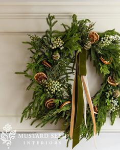 a christmas wreath hanging on the wall next to a door with green ribbon and pine cones