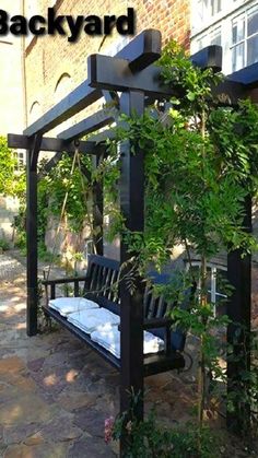 a black bench sitting under a pergoline covered arbor in front of a brick building