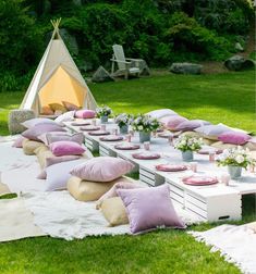 an outdoor picnic setting with pillows, plates and cups on the table in front of a teepee tent