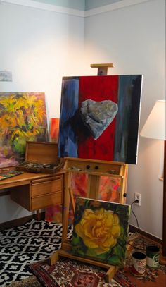 an artist's easel with paintings on it and a lamp next to it