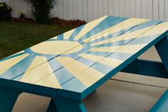 a blue and yellow picnic table sitting on top of a cement ground next to a white fence