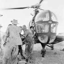 black and white photograph of men standing next to a helicopter with the pilot getting off