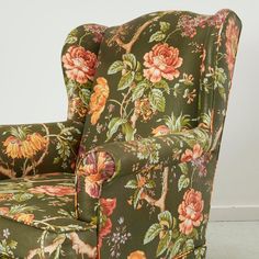 a green floral chair sitting on top of a hard wood floor next to a white wall