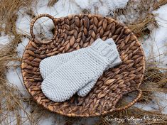 a knitted mitt sitting on top of a woven basket in the middle of snow