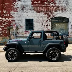 a green jeep parked in front of an old brick building with graffiti on the walls