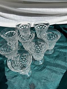 a group of glasses sitting on top of a green tablecloth covered bed sheet with white drapes in the background