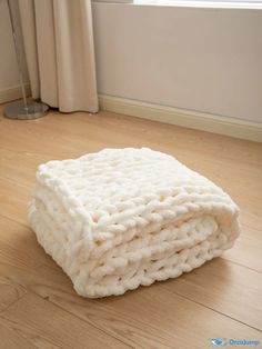 a white blanket sitting on top of a hard wood floor in front of a window