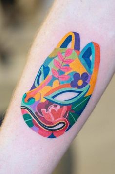 a colorful tattoo on the arm of a person with a cat mask painted on it