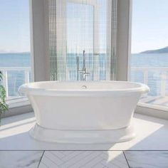 a white bath tub sitting on top of a tiled floor next to a large window