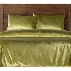 a bed with green sheets and pillows on top of it in a wooden headboard