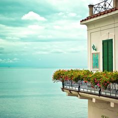 a balcony overlooking the ocean with green shutters and flower boxes on each window sill