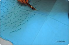 a person with a pen writing on a piece of blue paper that has wavy lines drawn across it