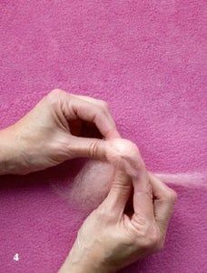 someone is sewing something on a pink surface with their hands and fingers touching the thread