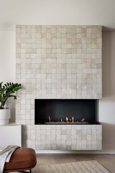 a modern fireplace in the middle of a living room with white tile walls and flooring