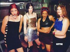 four young women standing in a kitchen with their arms around each other and wearing short skirts