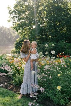 a woman holding a baby in her arms while standing next to flowers