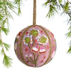 a pink ornament hanging from a tree branch with green leaves and flowers on it