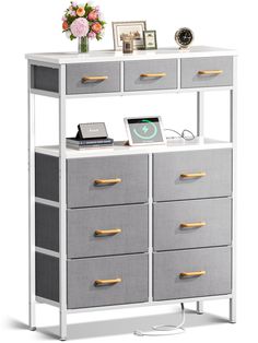 a white and gray dresser with drawers on it's sides, next to a flower vase