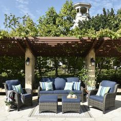 an outdoor seating area with blue and white pillows on the couches, under a pergolated roof