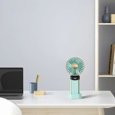 a laptop computer sitting on top of a desk next to a table with a fan