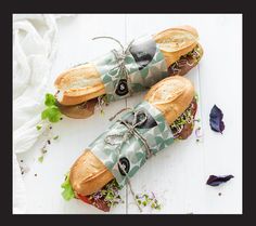 two sandwiches wrapped in paper and tied with twine on top of white wooden table