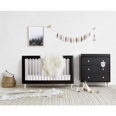 a baby crib in a white room with black dressers and rug on the floor