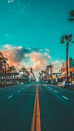 an image of a city street with palm trees and the sun setting in the background