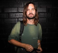 a man with long hair standing in front of a brick wall